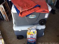 Two grey Coleman rolling ice chests stacked, with a bag of Kingsford charcoal and tarps placed on top, side view