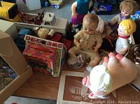 Photo showing dolls arranged on a table alongside a pink Babe the Pig toy, a Baby Pee Wee Nursery playset, and the Tonka truck in the background.