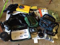 Full lot overview showing cameras, bags, lens case, and classic duffel bag on floor.