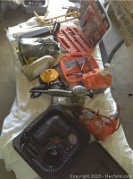 Photo showing various tools including a Black & Decker sander, air compressor, drill bits, and an orange fluid container arranged on a white cloth surface.