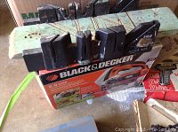 Black and orange Black & Decker orbital jigsaw in original box, placed on a table with a black plastic miter box on top showing rust stains.