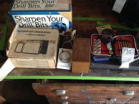 Overall view of boxed drill bit sharpeners and parts on a surface