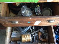 Wooden drawer holding metal trowel blades, various small tools, rope, and hardware items.