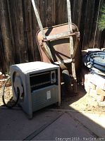 Photo showing metal wheelbarrow leaning against a wooden fence with the Ames Reel Easy hose cart in front, hose coiled inside the cart