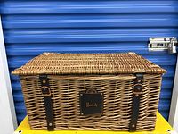 Front view of Harrods wicker picnic basket showing leather straps and plaque.