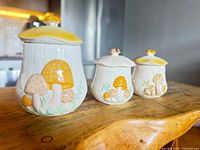 Three vintage ceramic kitchen storage jars with mushroom decoration displayed in size order