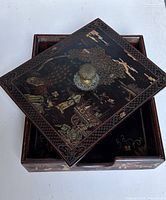 Lid angled on box showing brass knob and painted motifs