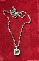 Full view of silver rope chain necklace with green halo pendant on red background