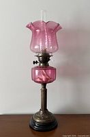 Full view of cranberry glass oil lamp on base