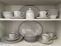 Complete set arranged in cabinet showing bowls, mugs, saucers, sugar bowl, platter and plates