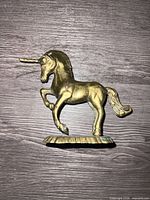 Side view of full brass unicorn figurine showing gold-tone finish and pedestal base