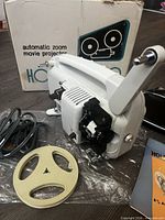 Projector with reel, cord, manual and box visible
