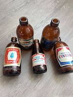 Five amber glass beer bottles with vintage labels displayed on floor