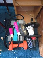 Pile view showing grey hex dumbbells, adjustable bar with plates, ab wheel, jump rope, neoprene dumbbells and straps