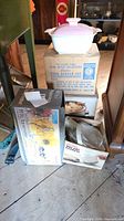 Stacked lot showing pink casserole on top of boxed buffet heater and other boxed items