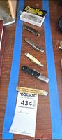 All six knives laid out on table with lot ticket visible