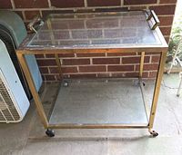Front angle of brass and glass bar cart showing two shelves and casters