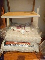 Stacked packaged bedding items on shelf: comforter, throw blanket, two pillow packages