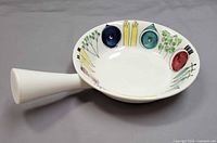 Top view of white ceramic frying pan showing vegetable motif and handle