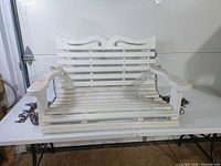 Front view of white wooden porch swing on table showing overall design and chains