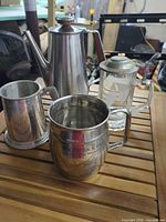 Group shot of stainless pot, two metal mugs, glass stein