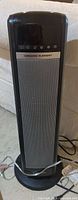 Full front view of black/gray tower heater with base and cord