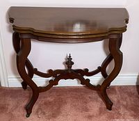 Front view of mahogany folding console table showing serpentine top, curved legs, stretcher, finial