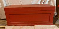 Front view of red wooden storage chest showing paneled front and base