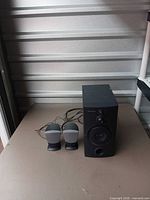 Subwoofer with two satellite speakers and cables on table