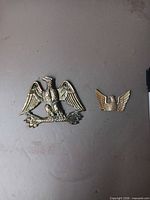 Both brass eagle plaques side by side on flat surface