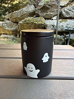 Front view of black metal canister showing ghost graphics and wood lid