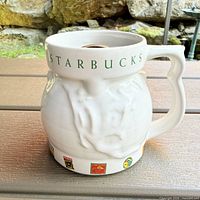 Front angled view of Starbucks mug showing handle, lid opening, textured body, and decals