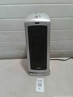 Front view of Lasko tower heater showing silver housing, black grille, top controls