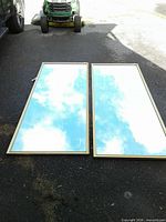 Two large rectangular mirrors on pavement reflecting sky