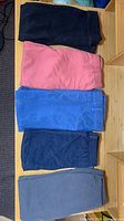 Five folded pairs of kids pants/leggings in black, coral pink, blue, dark denim and grey