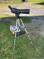 Scope mounted on tripod outdoors with box and carrying case visible