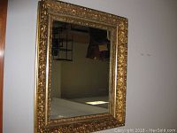 Full view of the rectangular gilt mirror with ornate frame showing gold-colored floral and scroll design detail with some wear on corners.