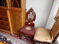 Photo showing the entire carved small decorative chair next to larger furniture for scale.
