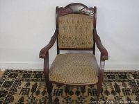Front view of the antique wooden armchair showing upholstery and armrests