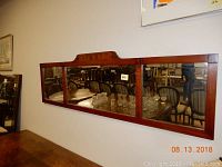 Front view of the wood framed antique triptych mirror showing three mirrored panels and ornate wooden crest on center panel.