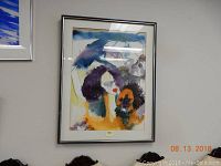 Framed abstract watercolor painting hung on wall with signature visible.