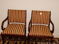 Pair of mid-century wooden chairs with curved armrests and striped upholstery, placed on patterned rug indoors.