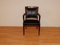 Front view of antique leather office chair with wooden frame and armrests.