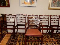 Wide shot showing six wooden dining chairs arranged in two rows. One chair is fully visible with a padded seat; other chairs have wooden seats and ladder-back detail with horizontal cut-outs.