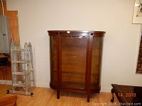 Full front view of the wooden curio cabinet with curved glass sides and door, showing the overall structure and wood finish.