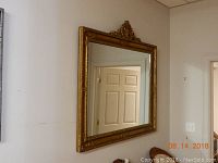Front view of the large rectangular mirror, showing the ornate and detailed gold-colored antique frame with decorative accents, and crest at the top center.