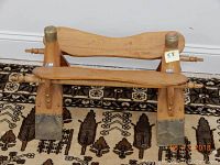 Wooden foot rest placed on a patterned carpet floor, showing the front view with brass foot protectors and curved top piece.