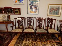 Overview of eight carved wooden dining chairs against wall with two armchairs flanking six side chairs