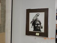 Full view of framed engraving mounted on wall showing a man wearing a knit cap with a parrot perched on his head.