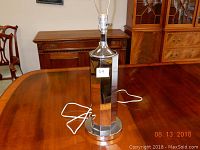 Mid century modern table lamp on wooden table with furniture in background. Chrome or polished metal octagonal base with white electrical cord.